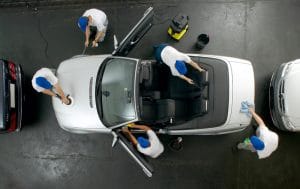 An overhead view of a white convertible car that is being professionally cleaned inside and out at an auto shop.