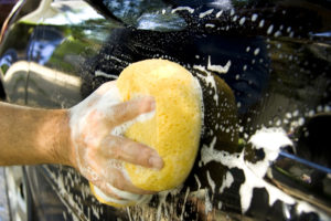Close-up view of a person washing their car with a big yellow sponge.