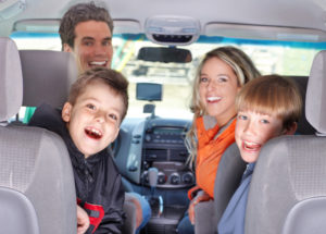 Family in a car before a trip all looking at the camera and smiling.